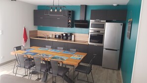 A modern kitchen with dark cabinets, a wooden dining table, and a stainless steel refrigerator. - New house for vacations in Charente-Maritime (Saint-Agnant)