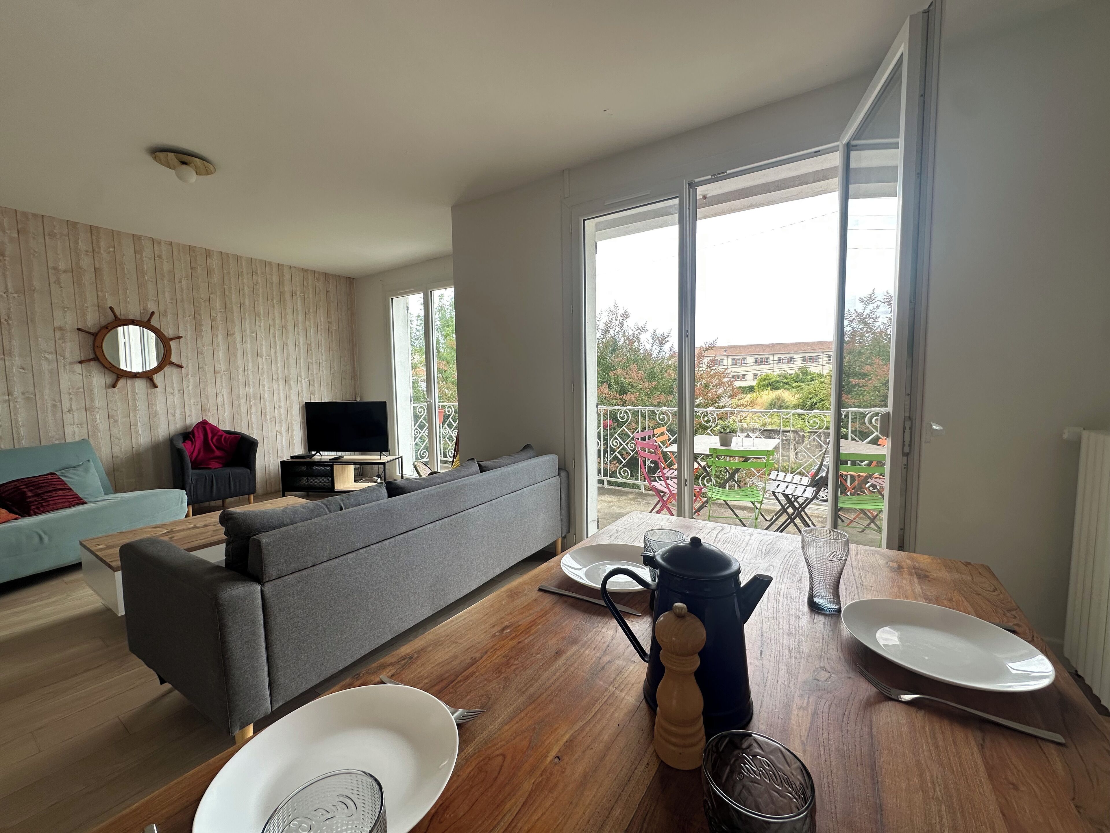 Ein modernes Wohnzimmer mit Sofa, Fernseher und Essbereich mit Tisch, Stühlen und Blick auf einen Balkon.