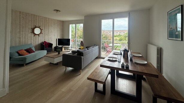 A modern living room with a sofa, TV, and dining area with a view of the outdoors.