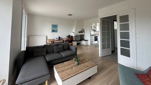 A modern living room with a grey sectional sofa, a wooden coffee table with a plant, and a dining area with a wooden table and chairs.