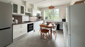 A modern kitchen with white cabinetry, a dining table with chairs, and a large window providing natural light.