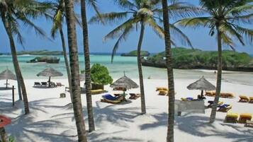 A beach with palm trees, lounge chairs, and umbrellas.
