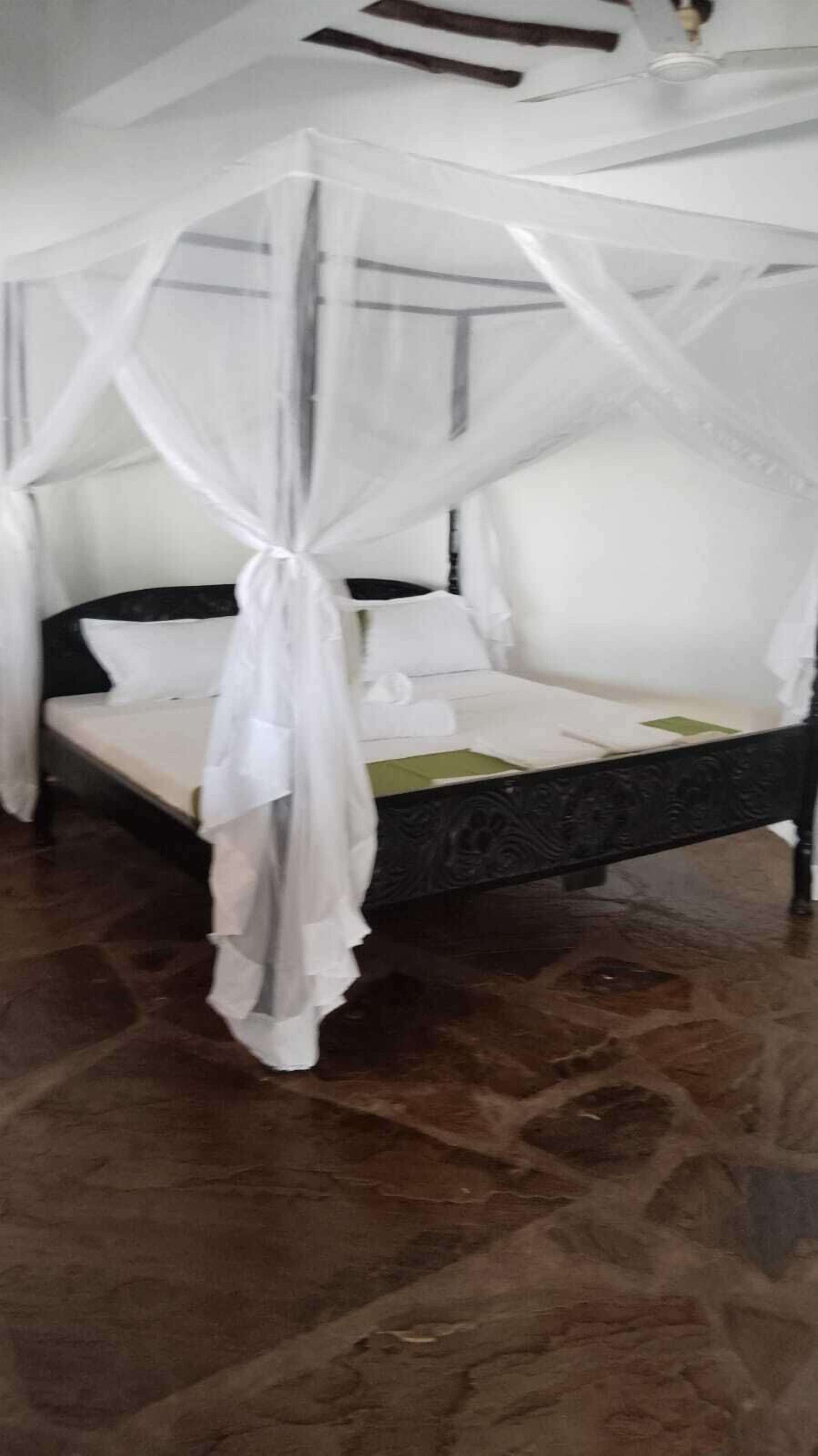 Un lit à baldaquin, un sol en pierre et un ventilateur de plafond.