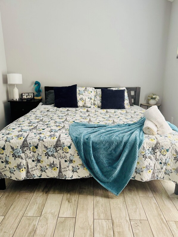 Una cama bien hecha con cubrecama con motivos de París, una manta color turquesa y un cojín estampado con flores.