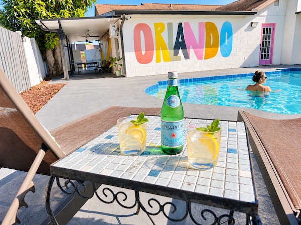 A poolside area with a table set for drinks, a bottle of S. Pellegrino water, and a person swimming in the pool.