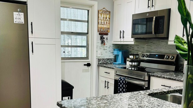A modern kitchen with white cabinets, a stainless steel refrigerator, a microwave, and a gas stove. - Charming 4-bedroom Pool house with WiFi, king bed, AC in lovely Orlando (Orlando)