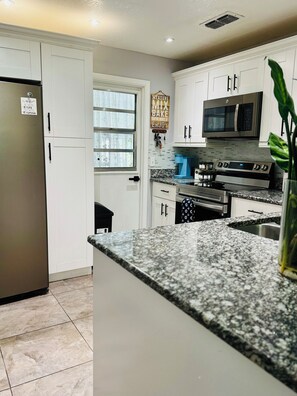 Una cocina moderna con armarios blancos, un refrigerador de acero inoxidable, un microondas y una estufa a gas.
