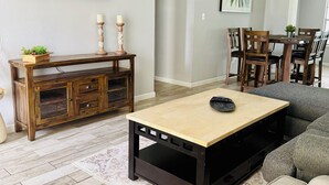 A living room with a wooden coffee table, a sofa, a TV mounted on the wall, and a dining area with chairs and a table. - Charming 4-bedroom Pool house with WiFi, king bed, AC in lovely Orlando (Orlando)