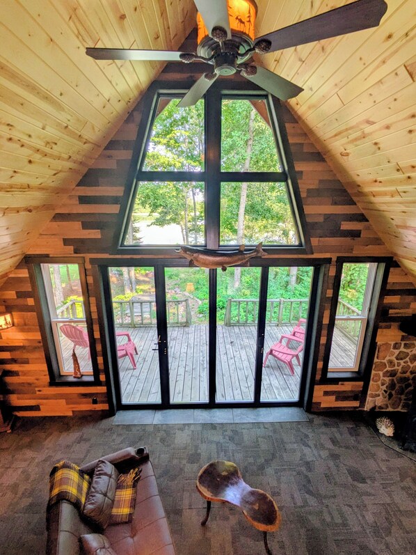 A room with a sloped ceiling, a ceiling fan, and a large window overlooking a deck.