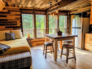 Interior rústico de uma cabana com uma cama, uma mesa de jantar e uma cozinha.
