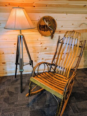 A wooden chair with a slatted seat and backrest, positioned next to a floor lamp with a conical shade, against a backdrop of wooden paneling.