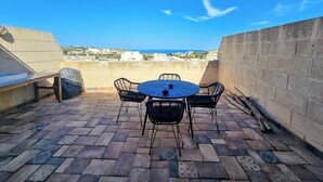 A patio with a round table and chairs, a barbecue grill, and a view of the sea. - GOZO APARTMENT (Qala)