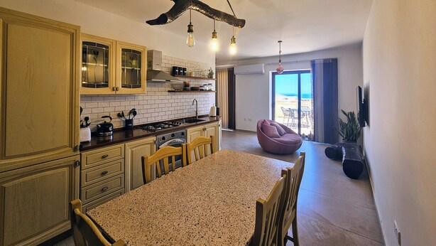 A kitchen with a dining area, wooden cabinets, a gas stove, and a hanging light fixture. - GOZO APARTMENT (Qala)