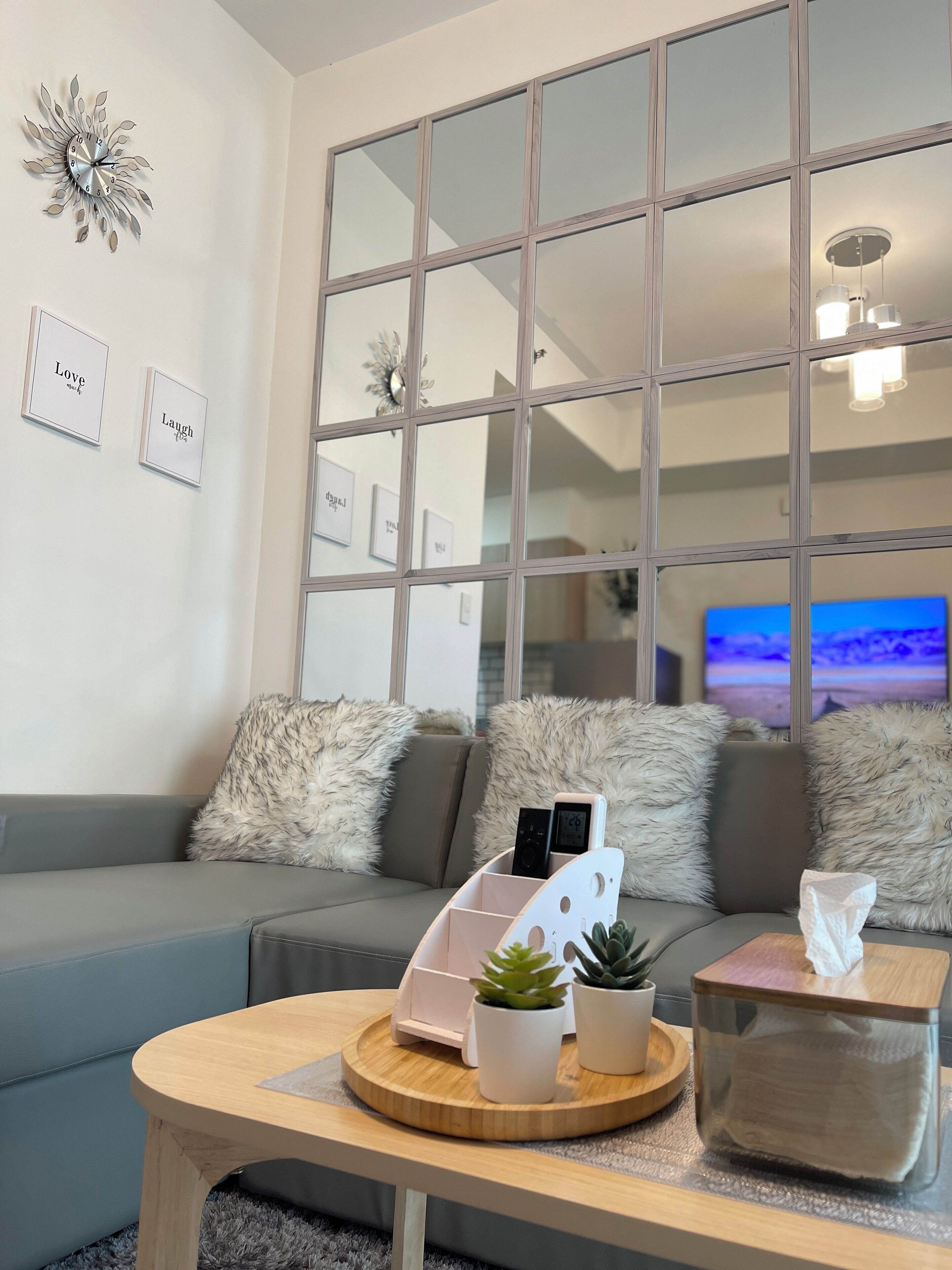 Un salon moderne avec un canapé gris, des coussins moelleux, une table basse en bois agrémentée de plantes, une station de recharge et un téléviseur en arrière-plan.