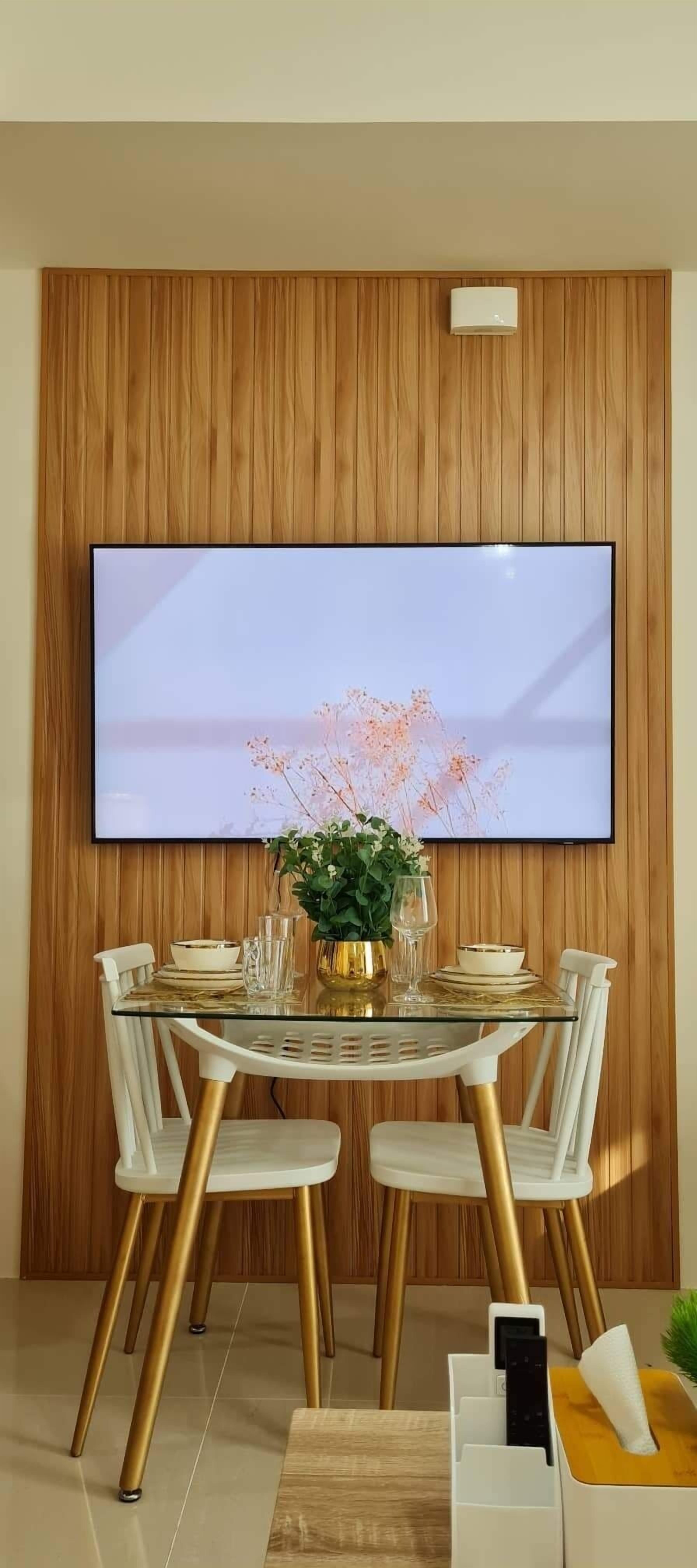 A dining area with a wooden panel wall, a flat-screen TV mounted above a table set for four, and a small plant on the table.