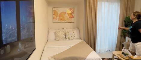 Ein Hotelzimmer mit einem Bett, einem Fernseher, einem Tisch mit Gläsern und einer Pflanze sowie einem Fenster mit Vorhängen.