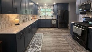 Una cucina moderna con mobili scuri, un'isola centrale, forno integrato e un tappeto a motivi.