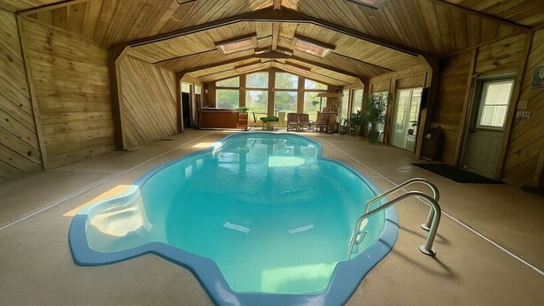 Una piscina interna con rivestimento in legno, un trampolino e vista sull'esterno attraverso ampie finestre.