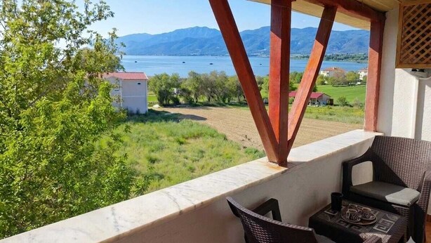 A balcony with a view of a lake and mountains, a table with chairs, and a small building in the background. - BEYSEHİR APART OTEL (Beysehir)