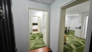 A hallway with a green carpet leading to a room with a bed and a chair. - BEYSEHİR APART OTEL (Beysehir)