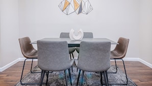 A dining area with a rectangular table, four grey upholstered chairs, a modern chandelier, and a geometric wall art piece. - Modern Columbus Haven Military  (Columbus)