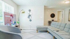 A modern living room with a sectional sofa, a grey armchair, a flat-screen TV, and a decorative wall piece. - Modern Columbus Haven Military  (Columbus)