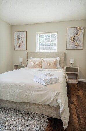 A bedroom with a large bed, two bedside tables, a window, and artwork on the walls. - Modern Columbus Haven Military  (Columbus)