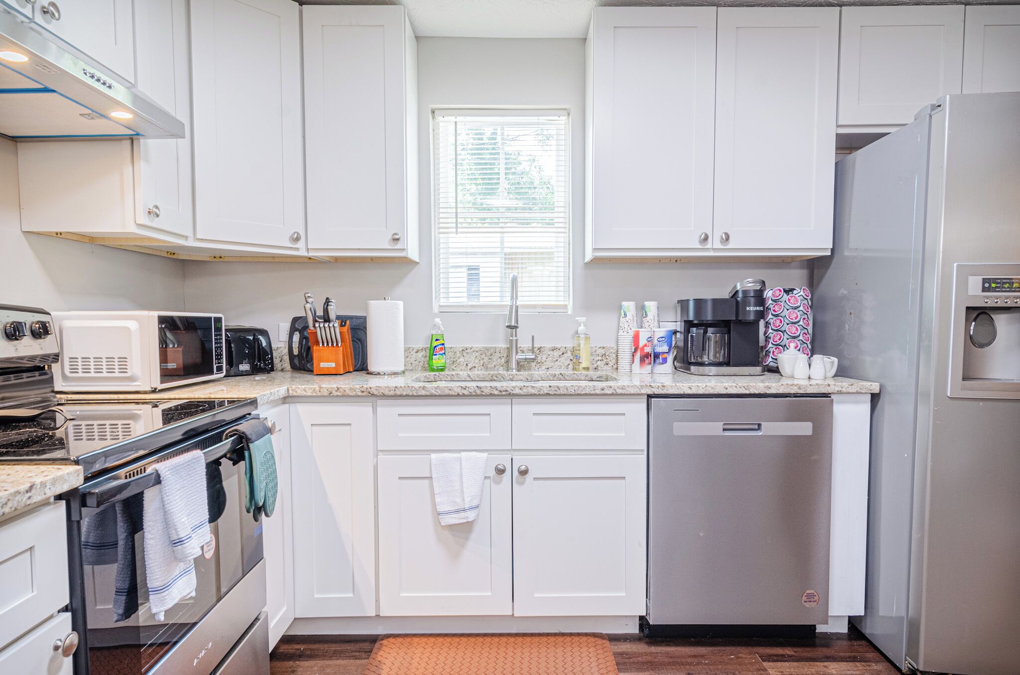 A modern kitchen with white cabinets, a stainless steel refrigerator, a dishwasher, a microwave, and a stove.