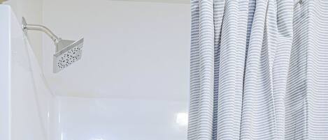 Un baño con una bañera blanca, un cabezal de ducha y una cortina con botones.