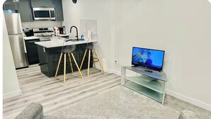 A modern living room with a grey sofa, a kitchen in the background, and a television on a stand. - Stylish One Bedroom Cozy Home (Edmonton)