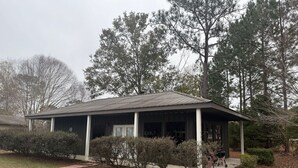 A single-story building with a covered porch, a garage, and a small front yard with shrubs.