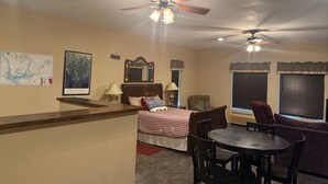 A room with a bed, a desk, a dining table, and two ceiling fans.