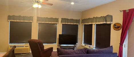 A living room with a ceiling fan, a flat-screen TV, a sofa, a chair, and a table.