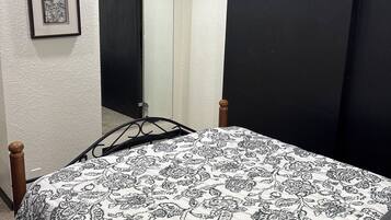 Une chambre à coucher avec un lit, un tableau encadré au mur, une porte et un luminaire au plafond.
