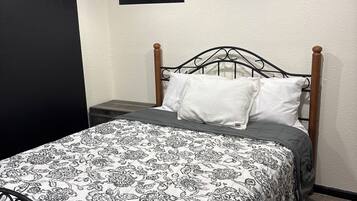 Una cama individual con un edredón estampado, cabecera de madera y estructura de metal negro.