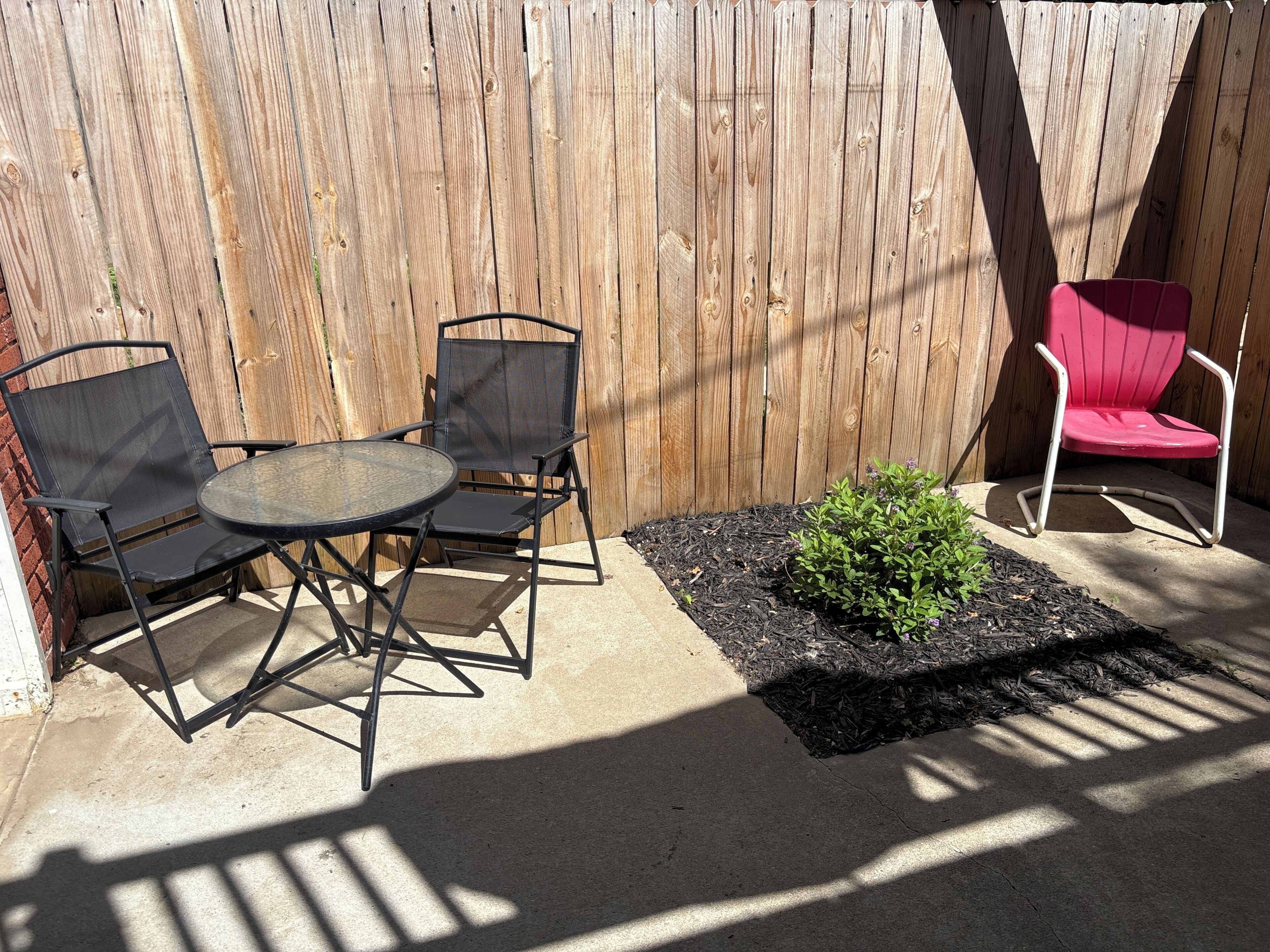 Une terrasse avec une table ronde et deux chaises, un petit pot de fleurs contenant des plantes vertes et une chaise rouge.