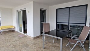 A room with a glass door leading to a balcony, a table with a yellow tablecloth, and a window with blinds.