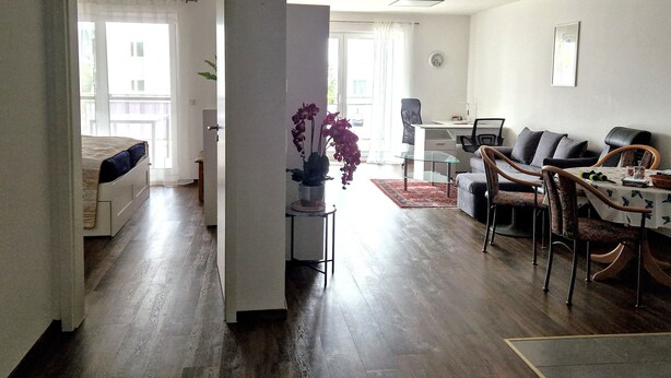 A spacious living area with a dining table, chairs, a sofa, and a small desk.