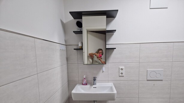 A bathroom with a white sink, a mirror, a toilet, and a trash bin.
