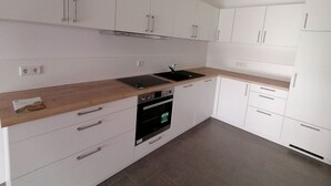 A modern kitchen with white cabinets, a wooden countertop, a black stove, and a built-in oven.
