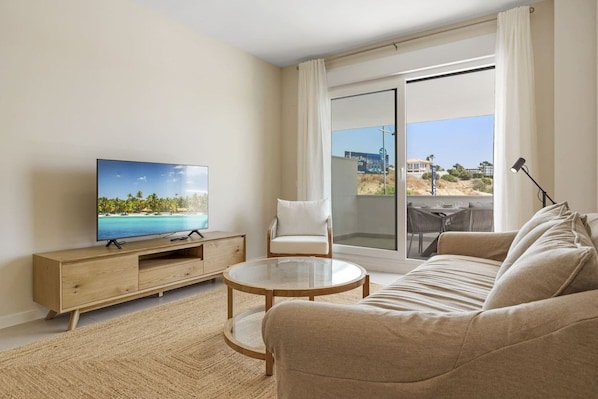 A modern living room with a flat-screen TV, a sofa, a glass coffee table, and a chair.
