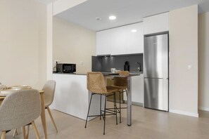 A modern kitchen with white cabinets, a stainless steel refrigerator, and a dining area with two chairs. - Indigo | Pool - gym - terrace (Estepona)