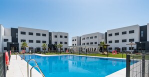 A swimming pool with a clear blue water surface, surrounded by a modern building with multiple floors and balconies.