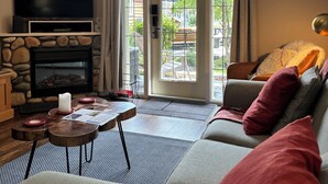 Een woonkamer met een open haard, een televisie, een bank en een eethoek met een tafel en stoelen.
