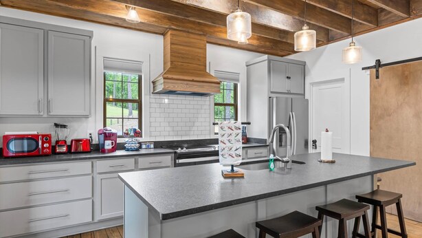 A modern kitchen with white cabinets, a large island, bar stools, and a stainless steel refrigerator. - Firefly Cottage, Firefly Cottage | Lake Martin Getaway | Sleeps 8 | Pet Friendly (Elmore County)