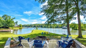 A lakeside deck with Adirondack chairs, a fire pit, and a view of the lake and surrounding greenery. - Firefly Cottage, Firefly Cottage | Lake Martin Getaway | Sleeps 8 | Pet Friendly (Elmore County)