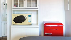 Une cuisine compacte équipée d’un four à micro-ondes, d’un réfrigérateur Galanz rouge et d’un meuble blanc aux portes en verre.