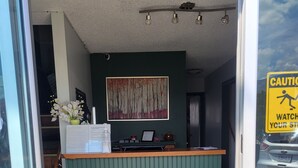 Un comptoir d’accueil avec un panneau vert, une œuvre d’art encadrée au-dessus et un panneau d’avertissement sur la fenêtre.