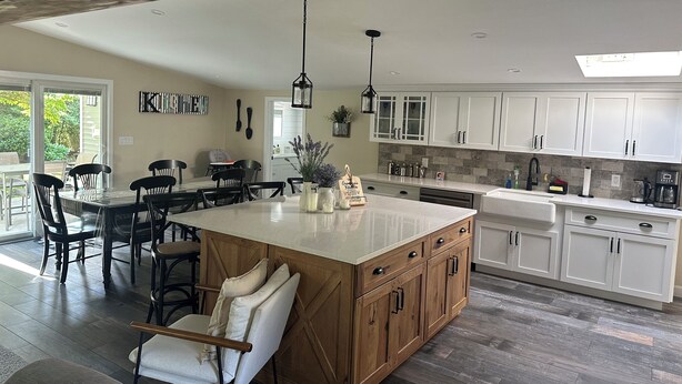 A modern kitchen with white cabinets, a large island, and a dining area with black chairs.
