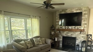 A living room with a beige sofa, a fireplace, a mounted TV, and a ceiling fan.